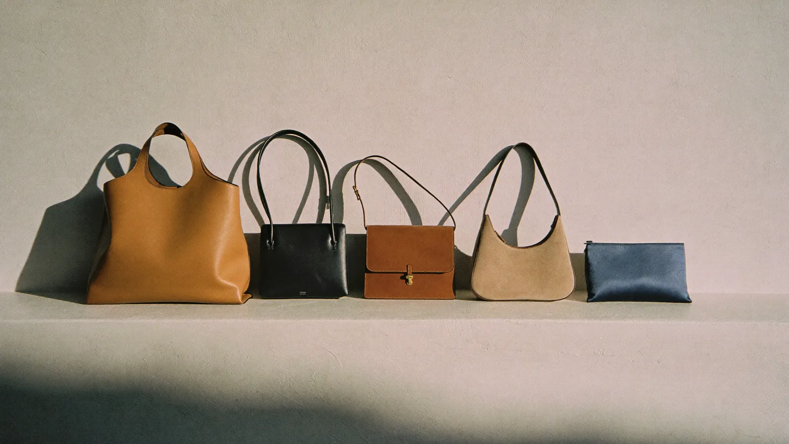 Fünf Damenhandtaschen nebeneinander auf einem hellen Sims: Shopper, Schultertasche, Crossbody, Hobo und Clutch.